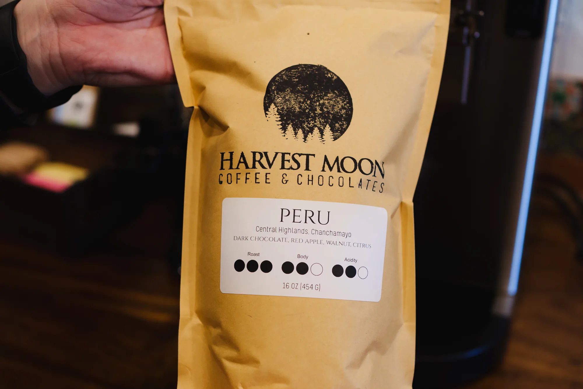 A hand holding a bag of Harvest Moon Peru coffee beside the grinder
